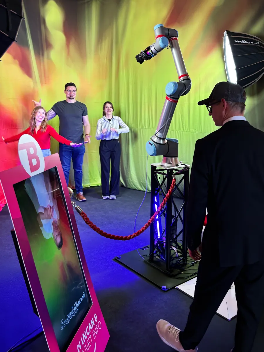 Glambot-Roboterarm mit Kamera bei einem Event, Gäste posieren davor
